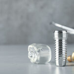 Dental implant pieces laying on a on a table, close up image of dental implant model. Reflecting off of the gloss table it shows all parts of a dental implants