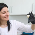 young woman holding dental implant mockup, artificial tooth roots into jaw canal. dental treatment concept