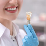 Dentist holding educational model of dental implant indoors, closeup.