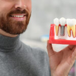 Man holding educational model of dental implant on blurred background, closeup